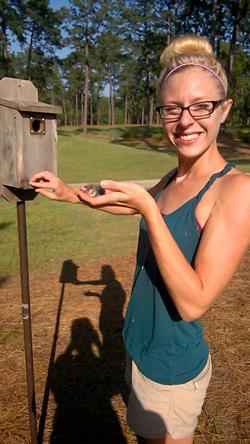 Dr. Lauren Gillespie holding a bird next to a birdhouse